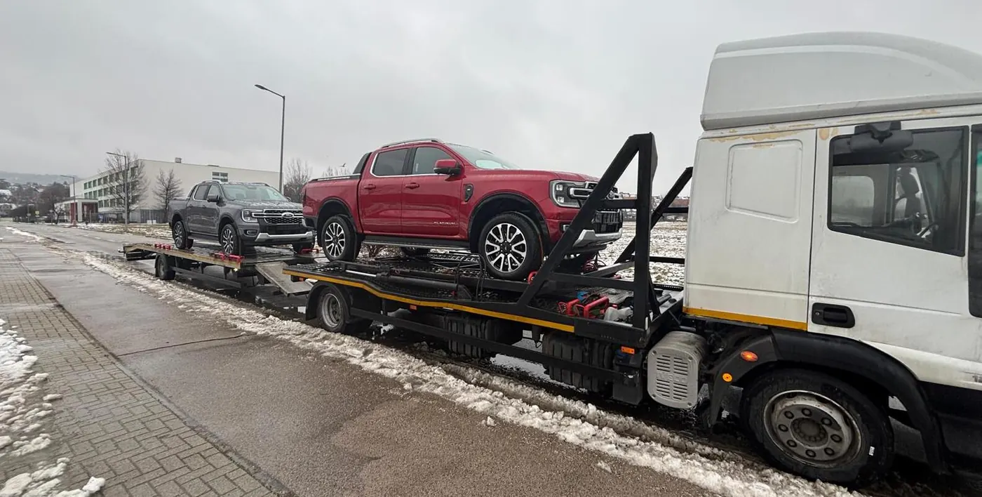 Autoprepravník s naloženými pickupmi na zasneženej ceste